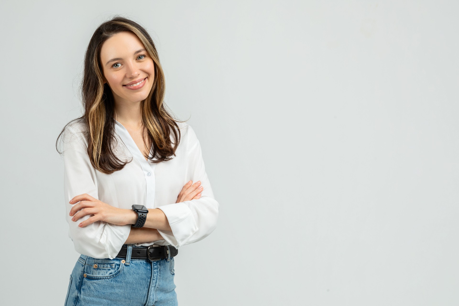 A confident young woman with long brunette hair smiles gently at the camera, arms crossed