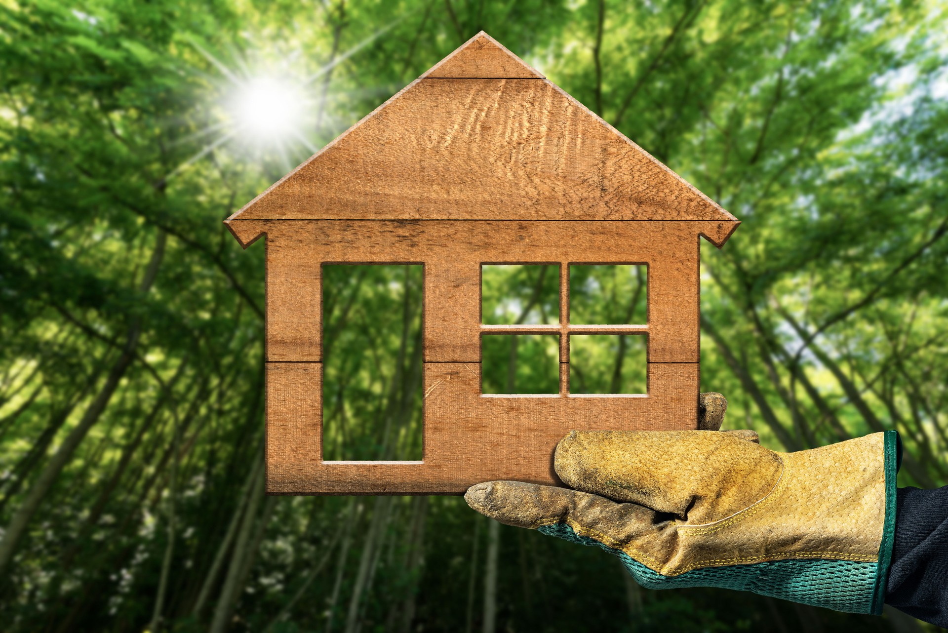 Hand with Work Glove Holding Holding a Small Wooden House in a Forest